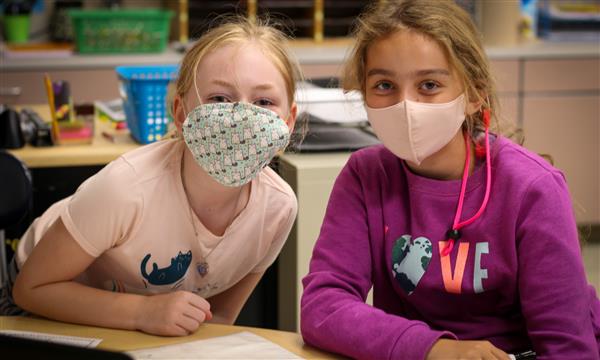 Two girls smile while wearing masks